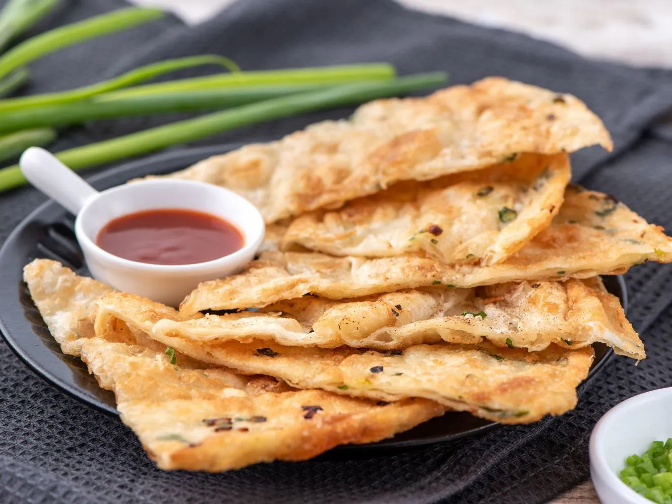 Crispy flaky scallion pancake sheets served with red dipping sauce at Authentic Yongtai Scallion Pie & Shi Wei BBQ, a Chinese Restaurant in Brooklyn