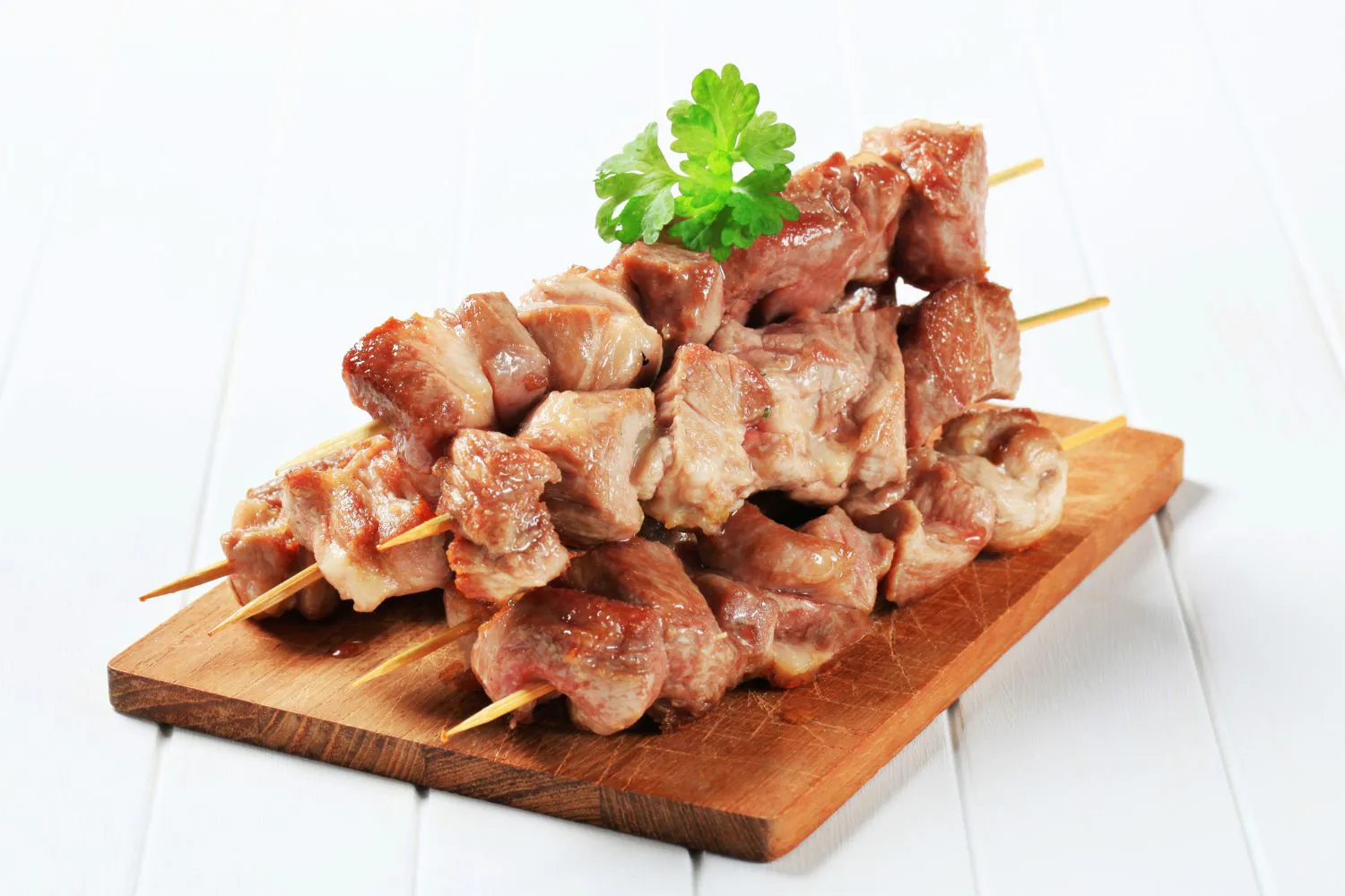 Plain grilled lamb skewers stacked on wooden board with parsley garnish at Authentic Yongtai Scallion Pie & Shi Wei BBQ, a Chinese Restaurant in Brooklyn